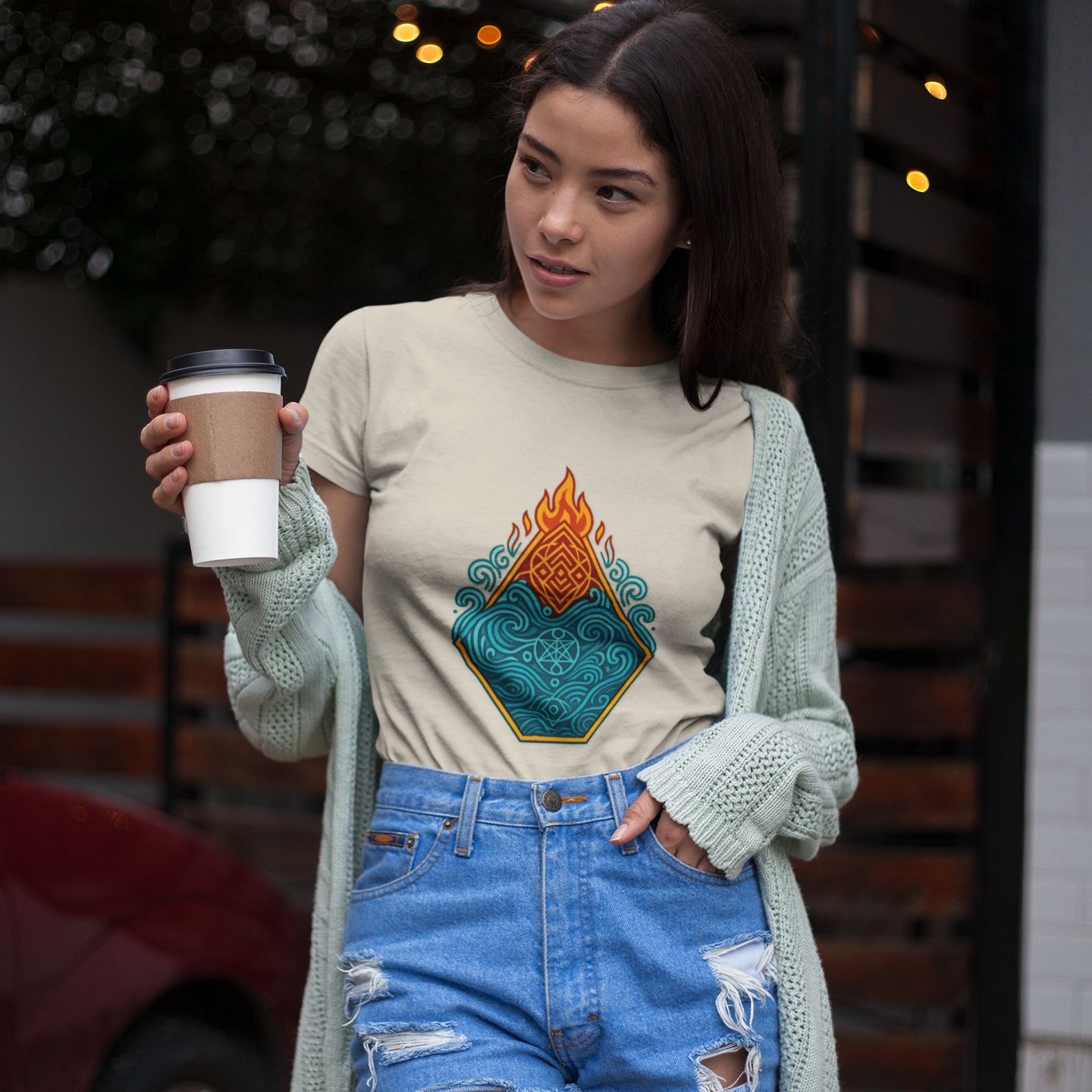 Woman holding a coffee cup, wearing a graphic t-shirt and denim shorts, standing outdoors.