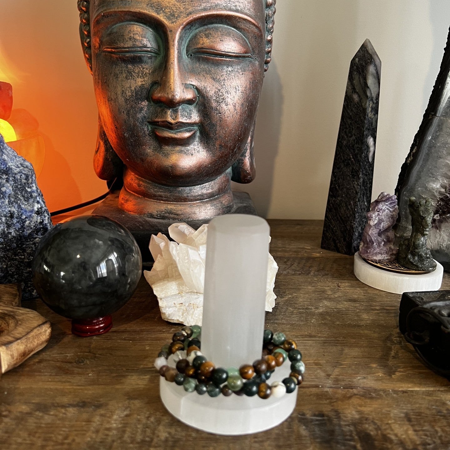 Decorative setup with a Buddha statue, crystal, and other stones on a wooden surface.